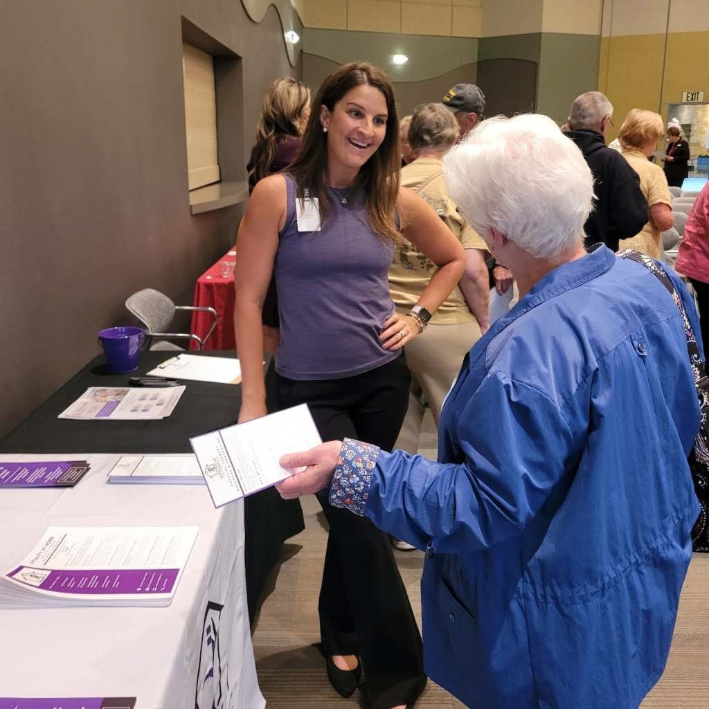 Dr. Jenna Smith at a community health fair, smiling as she hands a leaflet to an older woman