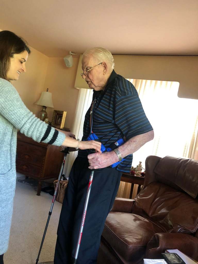 Dr. Jenna Smith helping an older client set up a pair of walking poles in his living room